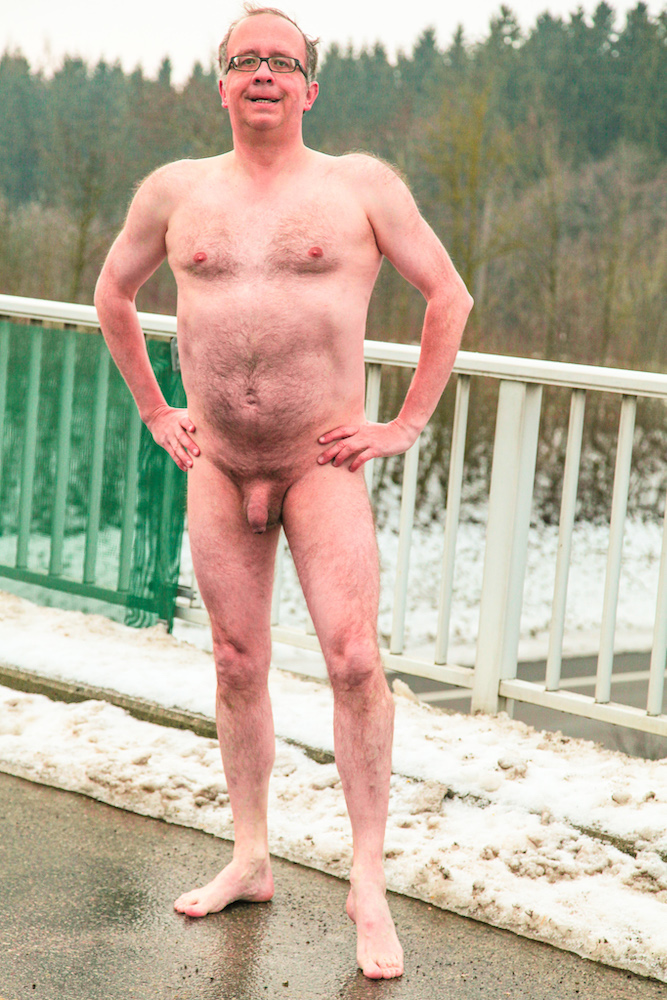 Stark naked man barefoot in the ice and snow on a bridge over a highway