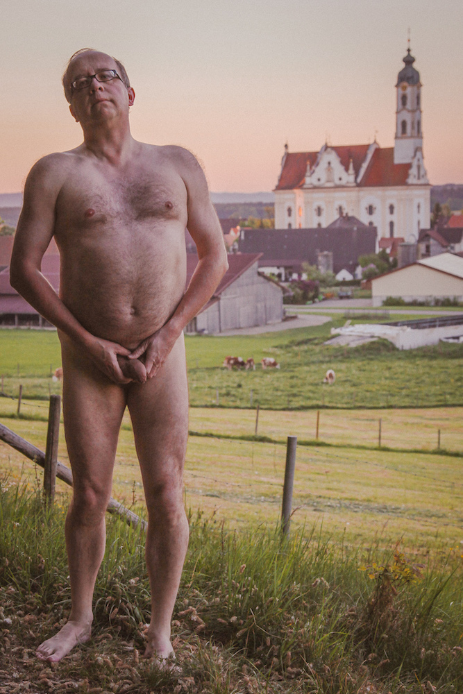 Stark naked man barefoot in front of a village