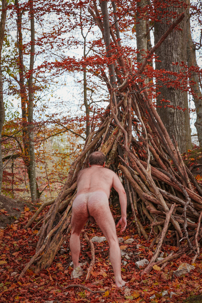 Stark naked man in the forest building a hut